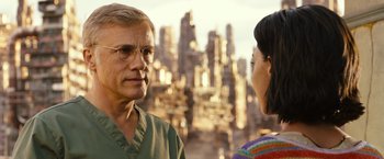 Movie still from “Alita: Battle Angel” (2019), directed by Robert Rodriguez – A man and a woman are standing in front of a city; Close Up shot, Over the shoulder angle
