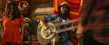 Movie still from “Alita: Battle Angel” (2019), directed by Robert Rodriguez – A man holding a guitar while sitting on a chair; Medium shot, Low angle