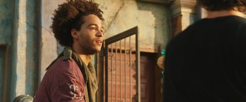 Movie still from “Alita: Battle Angel” (2019), directed by Robert Rodriguez – A young man with a beard is standing outside; Close Up shot, Over the shoulder angle