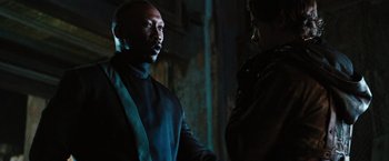 Movie still from “Alita: Battle Angel” (2019), directed by Robert Rodriguez – A man and a woman standing next to each other in the dark; Medium shot, Over the shoulder angle