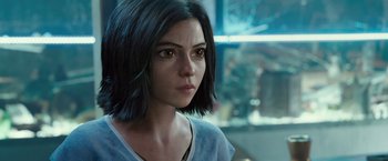 Movie still from “Alita: Battle Angel” (2019), directed by Robert Rodriguez – A person with short black hair; Close Up shot, Over the shoulder angle