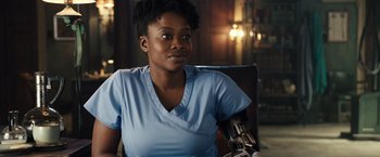 Movie still from “Alita: Battle Angel” (2019), directed by Robert Rodriguez – A woman sitting in a chair in a room; Close Up shot, Over the shoulder angle