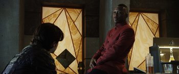 Movie still from “Alita: Battle Angel” (2019), directed by Robert Rodriguez – A man in a red coat is sitting next to a woman; Medium shot, Over the shoulder angle