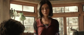Movie still from “Alita: Battle Angel” (2019), directed by Robert Rodriguez – A woman in a red jacket standing next to a window; Close Up shot, Over the shoulder angle