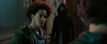 Movie still from “Alita: Battle Angel” (2019), directed by Robert Rodriguez – A man standing in front of a hooded figure; Close Up shot, Over the shoulder angle