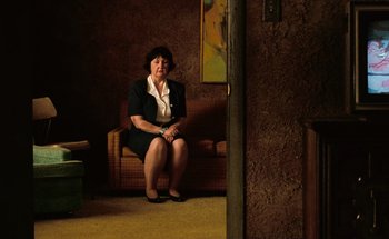 Movie still from “From Dusk Till Dawn” (1996), directed by Robert Rodriguez – An older woman sitting on a couch in a room; Wide shot, High angle