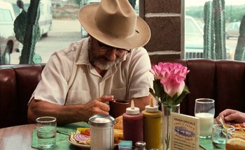 Movie still from “From Dusk Till Dawn” (1996), directed by Robert Rodriguez – An older man sitting at a table with a cup of coffee; Medium shot, Over the shoulder angle
