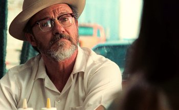 Movie still from “From Dusk Till Dawn” (1996), directed by Robert Rodriguez – A man with a hat and glasses sitting at a table; Close Up shot, Over the shoulder angle