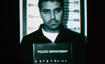 Movie still from “From Dusk Till Dawn” (1996), directed by Robert Rodriguez – A mugshot of a man in front of a police sign; Close Up shot, Overhead angle