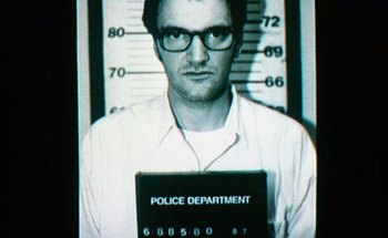 Movie still from “From Dusk Till Dawn” (1996), directed by Robert Rodriguez – A man with glasses is in front of a police department sign; Close Up shot, Low angle