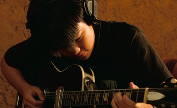 Movie still from “From Dusk Till Dawn” (1996), directed by Robert Rodriguez – A young man wearing headphones is playing an acoustic guitar; Close Up shot, Low angle