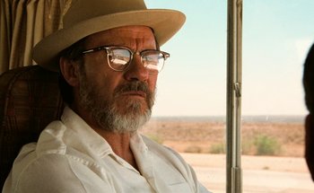 Movie still from “From Dusk Till Dawn” (1996), directed by Robert Rodriguez – An older man wearing a hat and glasses looking out a window; Close Up shot, Over the shoulder angle