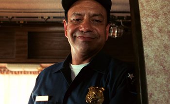 Movie still from “From Dusk Till Dawn” (1996), directed by Robert Rodriguez – A police officer smiling for the camera wearing a hat; Close Up shot, Low angle