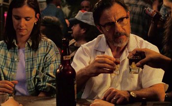 Movie still from “From Dusk Till Dawn” (1996), directed by Robert Rodriguez – An older man sitting at a table with a bottle of beer; Close Up shot, Over the shoulder angle