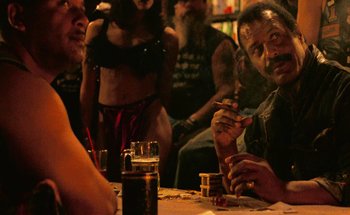 Movie still from “From Dusk Till Dawn” (1996), directed by Robert Rodriguez – A group of people sitting at a table with drinks; Medium shot, Over the shoulder angle