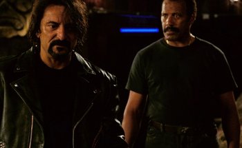 Movie still from “From Dusk Till Dawn” (1996), directed by Robert Rodriguez – Two men standing next to each other in a dark room; Medium shot, Over the shoulder angle