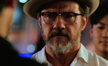 Movie still from “From Dusk Till Dawn” (1996), directed by Robert Rodriguez – A man with a beard wearing glasses and a hat; Close Up shot, Over the shoulder angle