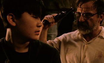 Movie still from “From Dusk Till Dawn” (1996), directed by Robert Rodriguez – A man with a beard and glasses combing a young boy's hair with an electric hair trimmer in front of him; Close Up shot, Over the shoulder angle