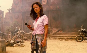 Movie still from “From Dusk Till Dawn” (1996), directed by Robert Rodriguez – A woman holding a cell phone while standing in the dirt; Medium shot, Low angle
