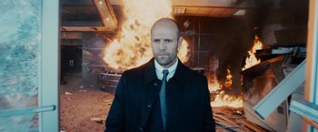 Movie still from “Furious 7” (2015), directed by James Wan – A bald man in a black jacket and a tie in front of an explosion; Close Up shot, Low angle