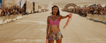 Movie still from “Furious 7” (2015), directed by James Wan – A woman in a pink top holding a pink scarf; Medium shot, Low angle