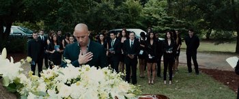 Movie still from “Furious 7” (2015), directed by James Wan – A group of people standing next to each other in front of a white casket; Wide shot, Over the shoulder angle