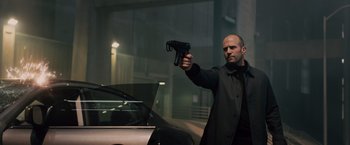Movie still from “Furious 7” (2015), directed by James Wan – A man holding a gun in front of a parked car; Medium shot, Low angle