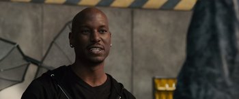Movie still from “Furious 7” (2015), directed by James Wan – A man with a black shirt is smiling for the camera; Close Up shot, Over the shoulder angle