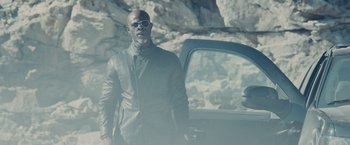 Movie still from “Furious 7” (2015), directed by James Wan – A man standing in front of a car in front of a mountain; Medium shot, Low angle