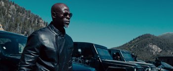 Movie still from “Furious 7” (2015), directed by James Wan – A man in a leather jacket standing in front of some cars; Medium shot, Low angle