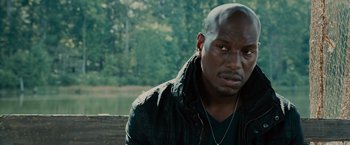 Movie still from “Furious 7” (2015), directed by James Wan – A man sitting on top of a bench near a body of water; Close Up shot, Over the shoulder angle