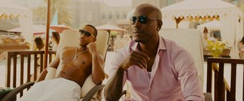 Movie still from “Furious 7” (2015), directed by James Wan – Two men sitting on lounge chairs next to each other; Medium shot, Over the shoulder angle