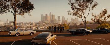 Movie still from “Furious 7” (2015), directed by James Wan – A group of people standing in a parking lot with cars parked in front of them; Extreme Wide shot, High angle