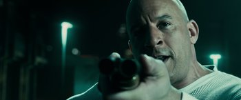 Movie still from “Furious 7” (2015), directed by James Wan – A man holding a gun pointed to the side of his face; Close Up shot, Over the shoulder angle