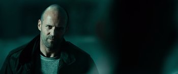 Movie still from “Furious 7” (2015), directed by James Wan – A man with a bald head is standing in a dark room; Close Up shot, Over the shoulder angle