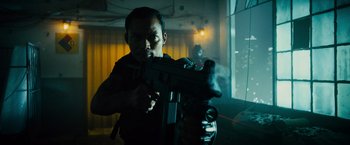 Movie still from “Furious 7” (2015), directed by James Wan – A man holding a gun while standing next to a window; Medium shot, Low angle