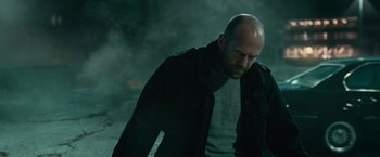 Movie still from “Furious 7” (2015), directed by James Wan – A bald man in a black jacket is looking down; Medium shot, Low angle