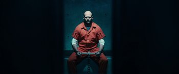 Movie still from “Furious 7” (2015), directed by James Wan – A man in a red jumpsuit sitting on a bench with chains; Wide shot, Low angle