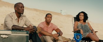 Movie still from “Furious 7” (2015), directed by James Wan – A man sitting on the ground next to another man; Medium shot, Low angle