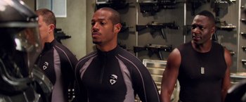 Movie still from “G.I. Joe: The Rise of Cobra” (2009), directed by Stephen Sommers – A man in a black and gray shirt and some other men; Medium shot, Over the shoulder angle