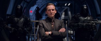 Movie still from “G.I. Joe: The Rise of Cobra” (2009), directed by Stephen Sommers – A man in a suit and tie standing with his arms crossed; Medium shot, Low angle