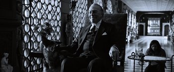 Movie still from “All the Money in the World” (2017), directed by Ridley Scott – An older man sitting in a chair with a dog; Medium shot, Low angle