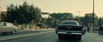 Movie still from “All the Money in the World” (2017), directed by Ridley Scott – A car driving down a street past trees and buildings; Wide shot, Low angle