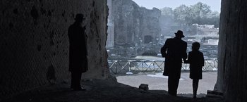 Movie still from “All the Money in the World” (2017), directed by Ridley Scott – Two men standing next to each other in front of a stone wall; Wide shot, Over the shoulder angle