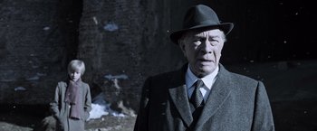Movie still from “All the Money in the World” (2017), directed by Ridley Scott – An older man in a suit and hat is standing in front of a stone wall; Close Up shot, Low angle