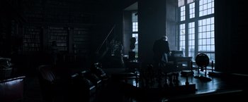 Movie still from “All the Money in the World” (2017), directed by Ridley Scott – A man sitting in a dark room next to a staircase; Wide shot, High angle