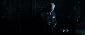 Movie still from “All the Money in the World” (2017), directed by Ridley Scott – An older man in a suit and tie looking at a cell phone in front of a book shelf; Medium shot, Low angle