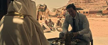 Movie still from “All the Money in the World” (2017), directed by Ridley Scott – A group of men sitting around a table with a camel in the background; Medium shot, Over the shoulder angle
