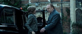 Movie still from “All the Money in the World” (2017), directed by Ridley Scott – A man and a woman standing next to each other in front of a car; Medium shot, Low angle