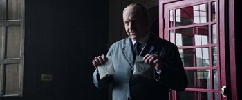 Movie still from “All the Money in the World” (2017), directed by Ridley Scott – A man in a suit and tie holding a bag of food; Close Up shot, Over the shoulder angle